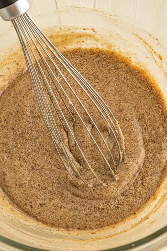 A whisk in a bowl with a brown mixture.