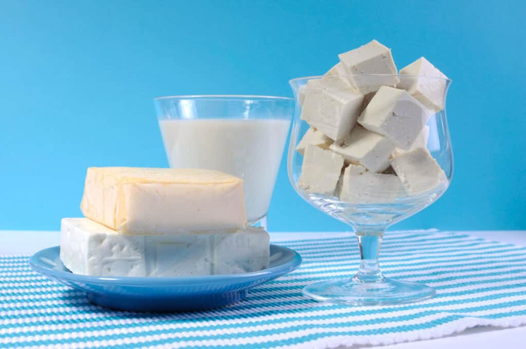 A glass of milk and a piece of tofu on a blue tablecloth.