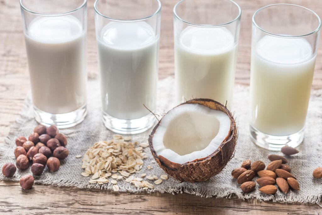 A glass of milk, almonds, and oats on a wooden table.