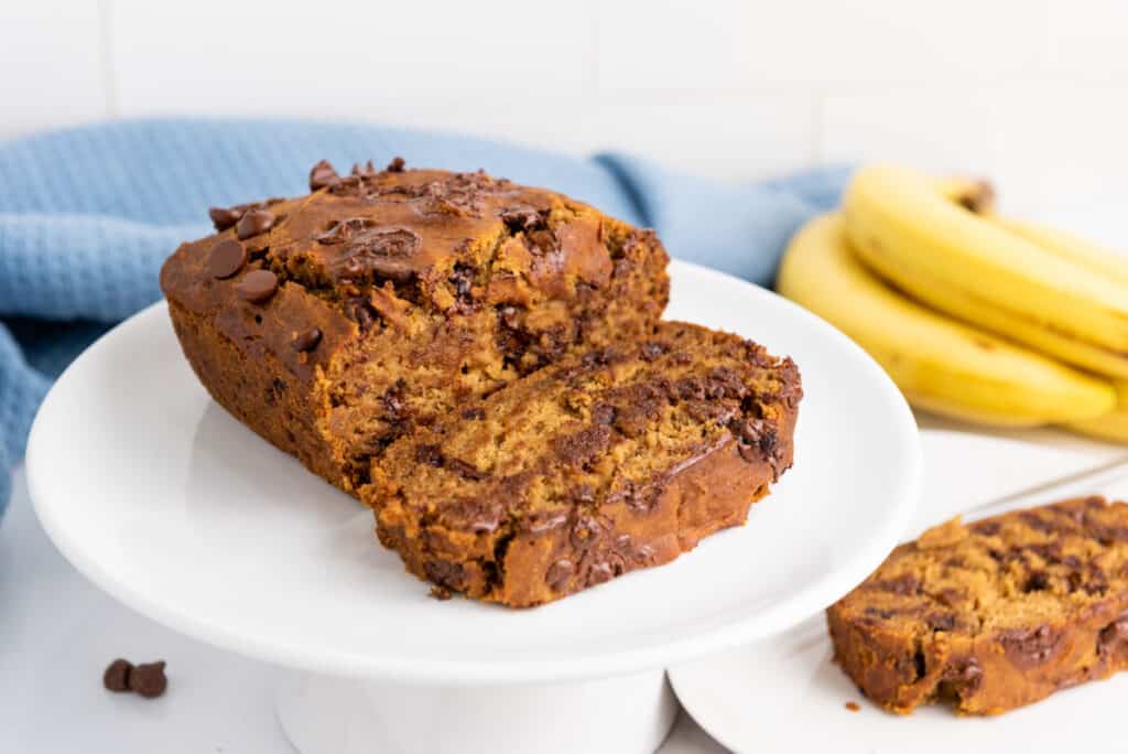 Gluten-Free Chocolate Chip Banana Bread on a white plate with bananas.
