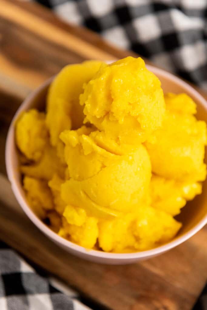 A bowl of yellow mango sorbet on a wooden cutting board.