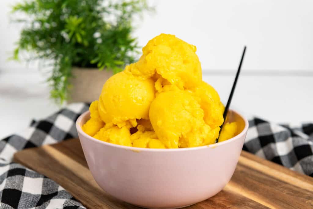A bowl of mango sorbet with a spoon.