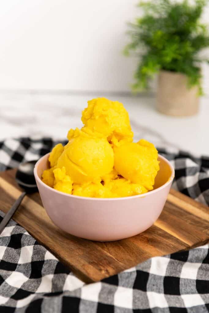 A bowl of yellow mango sorbet on a wooden cutting board.