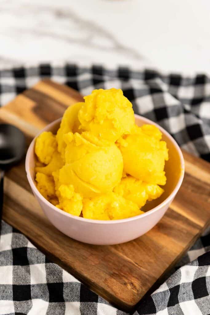 A bowl of mango sorbet on a wooden cutting board.