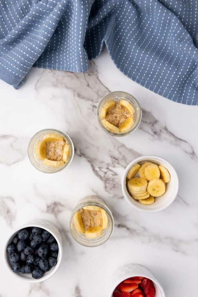 Four bowls of oatmeal with berries and bananas on a marble table.