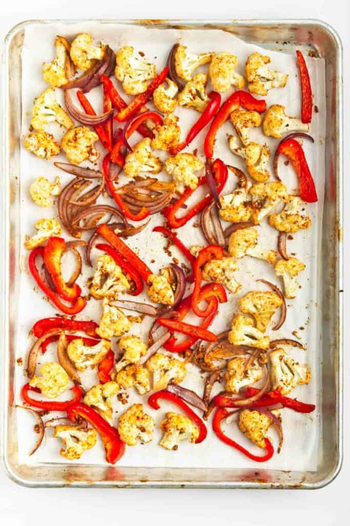 Roasted cauliflower tacos with red peppers on a baking sheet.