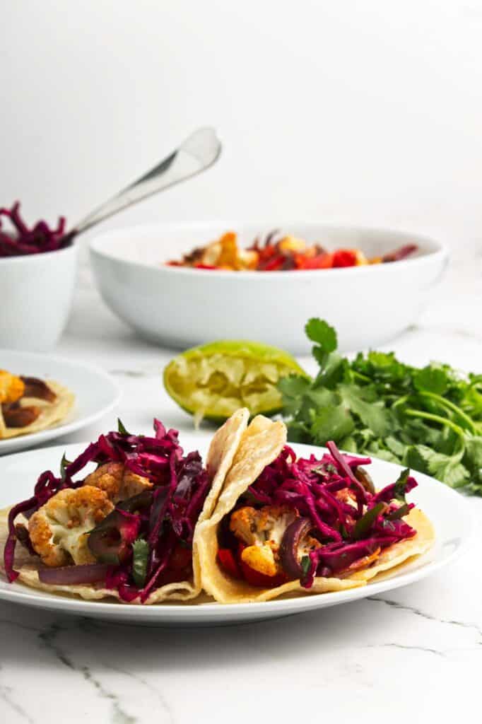 Two plates of roasted cauliflower tacos with red cabbage on them.