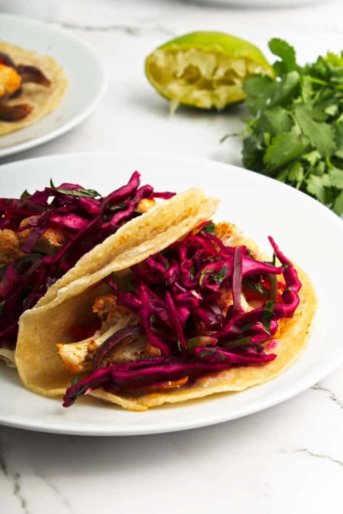 Two roasted cauliflower tacos with red cabbage and cilantro on a white plate.