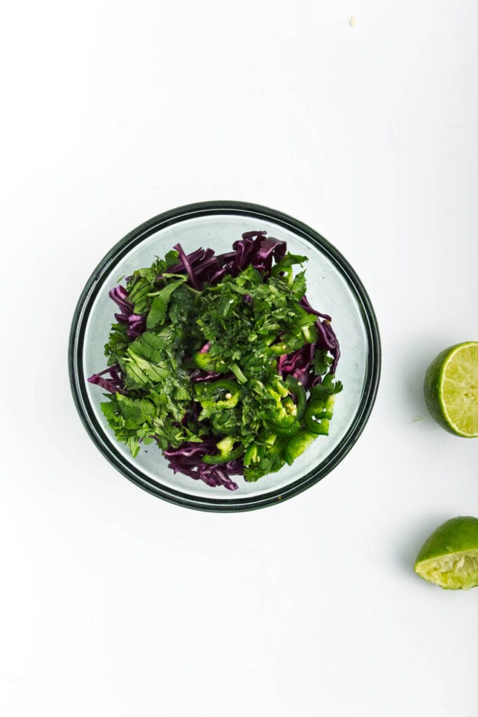 A bowl of cilantro and red cabbage next to limes.