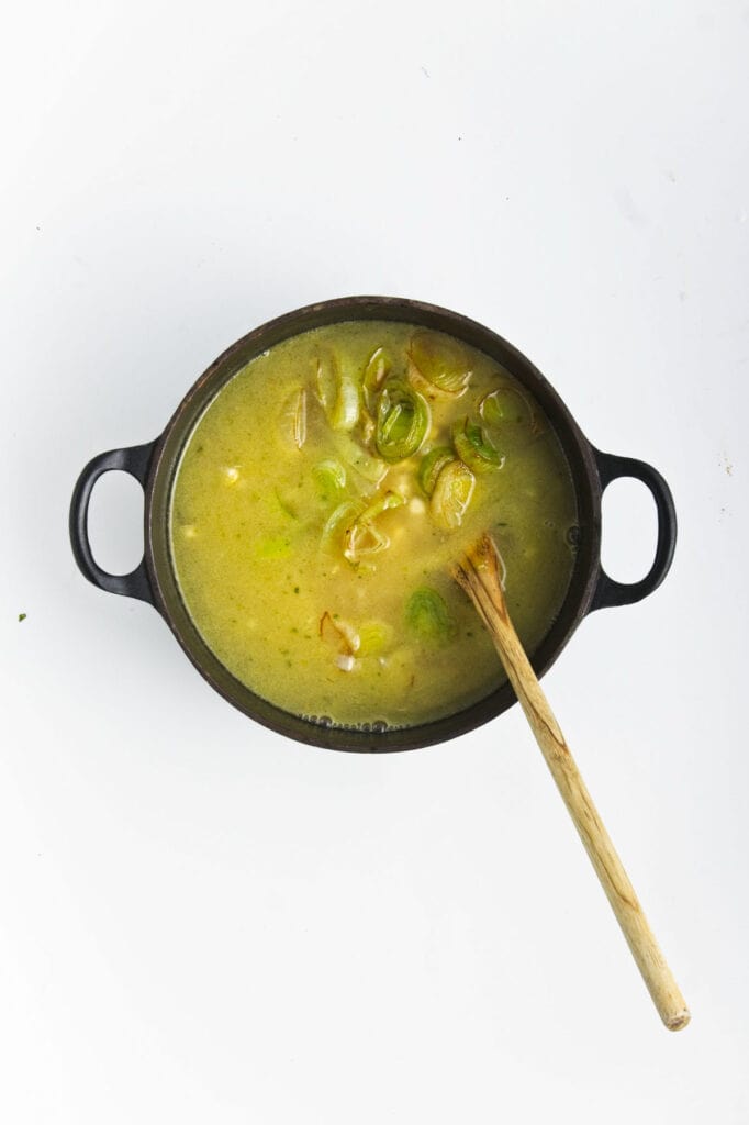 A pot with rice and vegetable stock for a sweet corn and leek risotto dish.