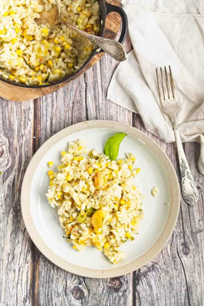 A plate of sweet corn and leek risotto on a wooden table.