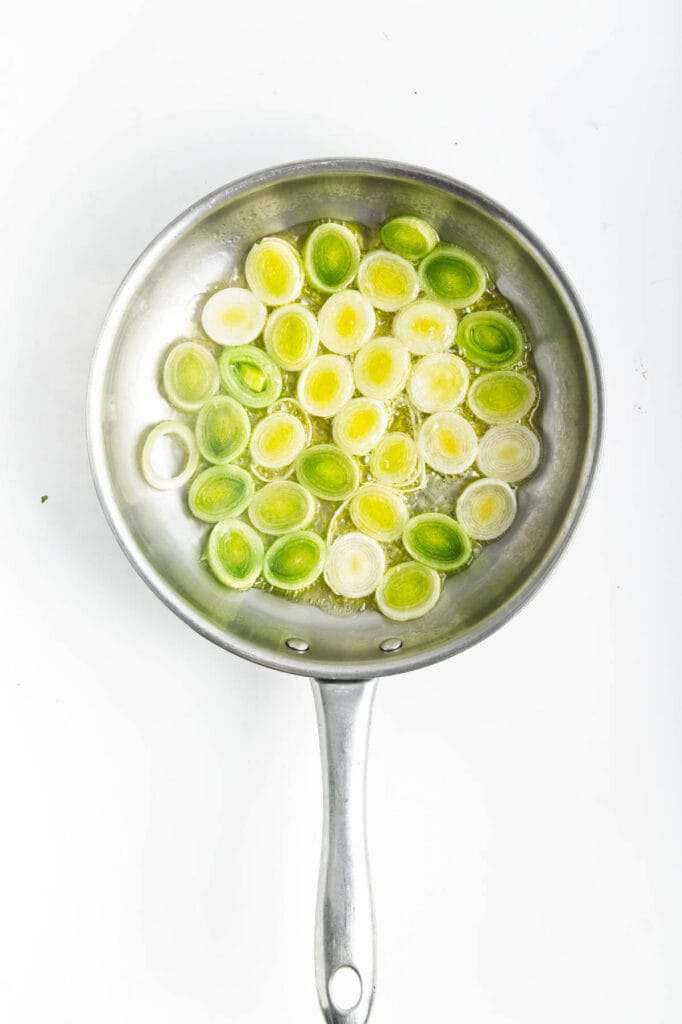 Sliced leek rounds in a frying pan on a white background.