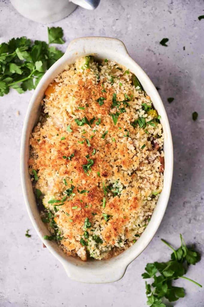 Baked vegetable casserole dish topped with breadcrumbs and garnished with fresh herbs, served on a kitchen countertop.