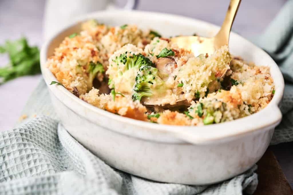 A Vegetable Casserole dish filled with broccoli and mushrooms topped with a golden breadcrumb crust.