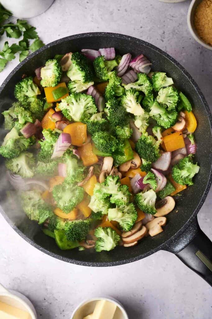 A skillet with a colorful vegetable casserole of broccoli, bell peppers, onions, and mushrooms on a kitchen counter.