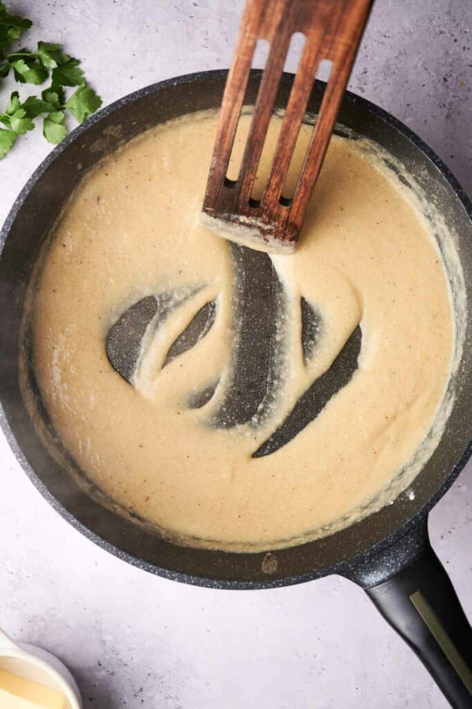 Creamy sauce for a vegetable casserole being stirred in a pan with a wooden spatula.