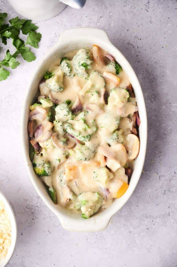 A vegetable casserole with broccoli and cheese topping in a white ceramic dish.