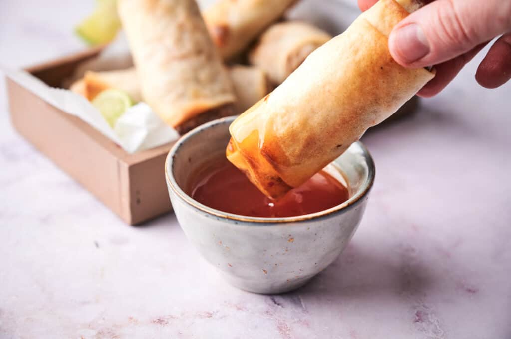 A vegan egg roll dipped into a sauce cup.