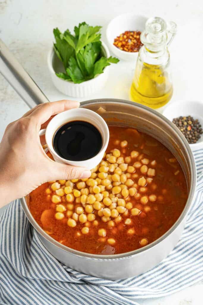 A person holding a bowl of chickpeas in a pan.