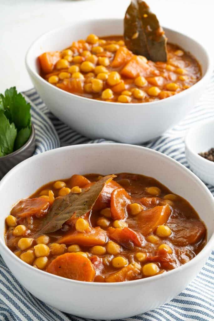 Two bowls of stew with carrots and beans.