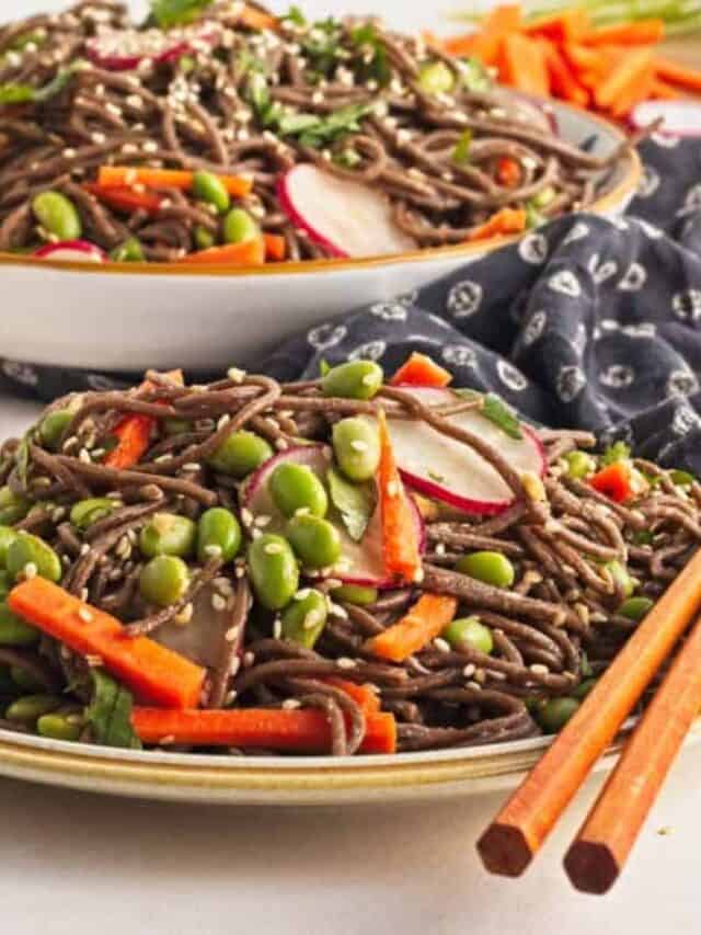 A bowl of soba noodle salad with vegetables and edamame, served with chopsticks on the side.
