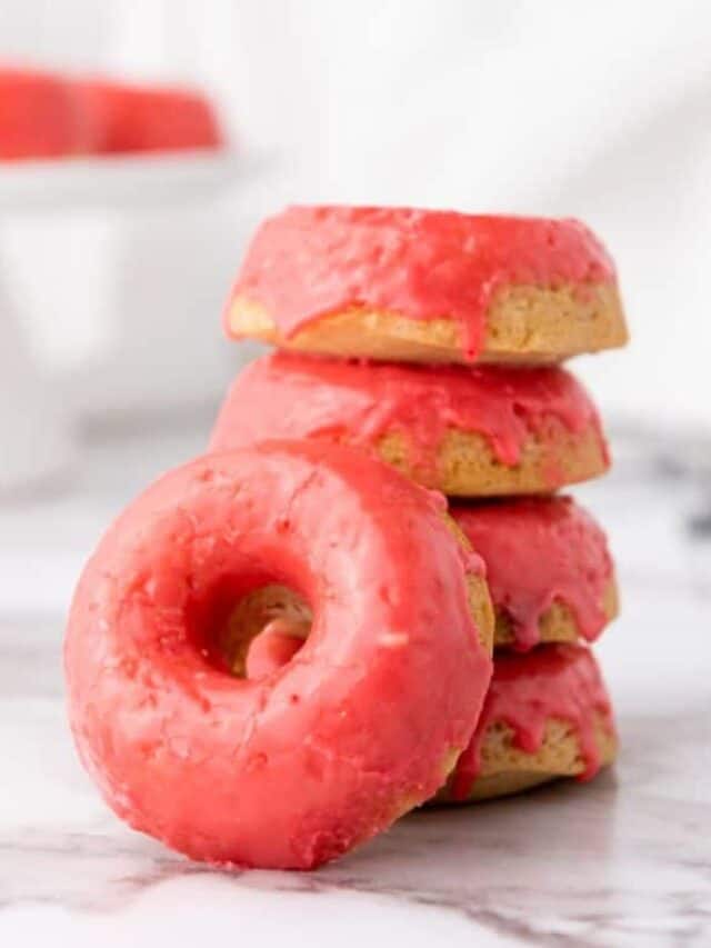 A stack of pink-frosted donuts on a white surface.