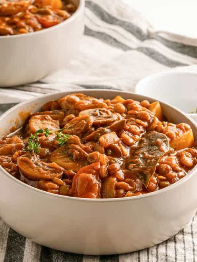 A bowl of hearty beef and bean stew garnished with fresh herbs.