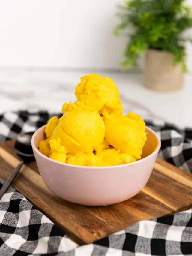A bowl of yellow ice cream on a wooden cutting board.