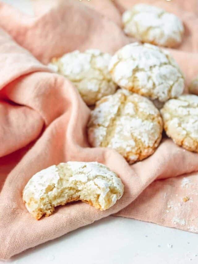 A collection of powdered sugar-coated cookies on a pink cloth, with one cookie suggestively bitten into.