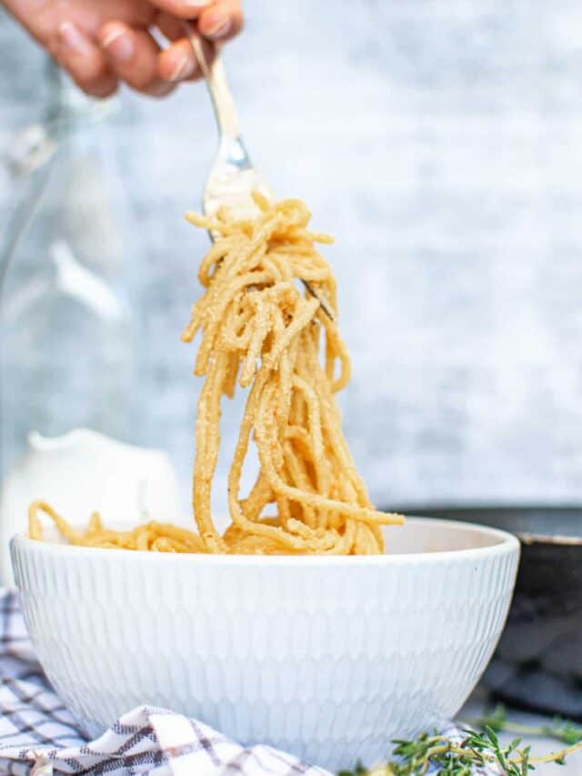 A person twirling a fork with golden, thin noodles over a white bowl.