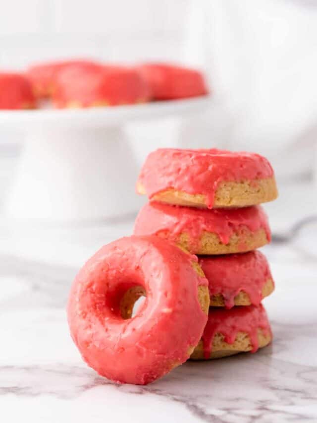 A stack of pink-frosted doughnuts on a marble surface.