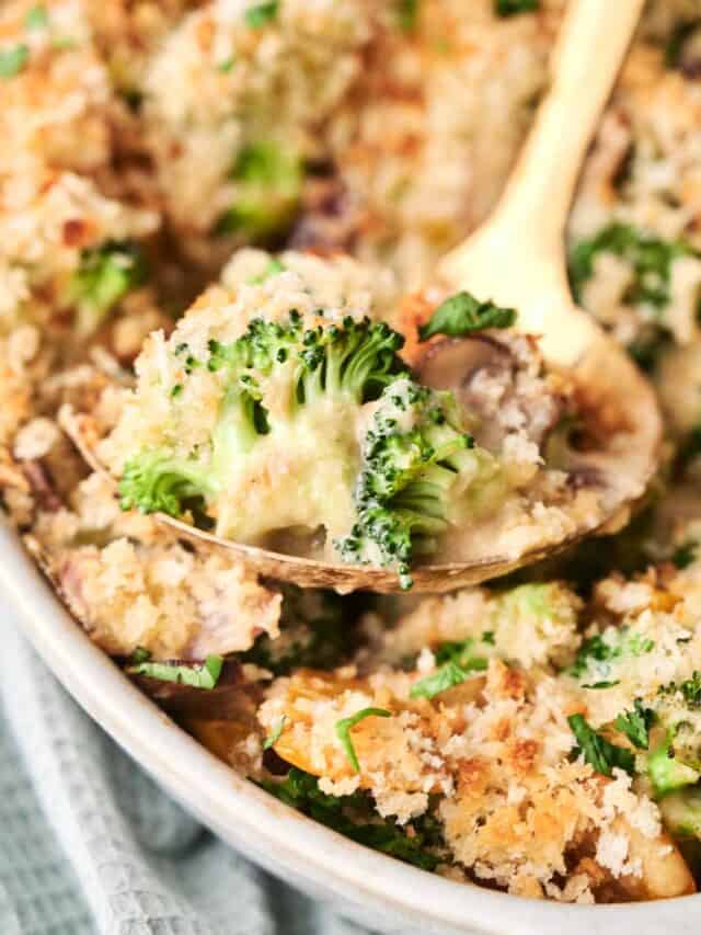 A close-up view of a broccoli casserole dish with a creamy filling and a golden-brown breadcrumb topping, being served with a spoon.