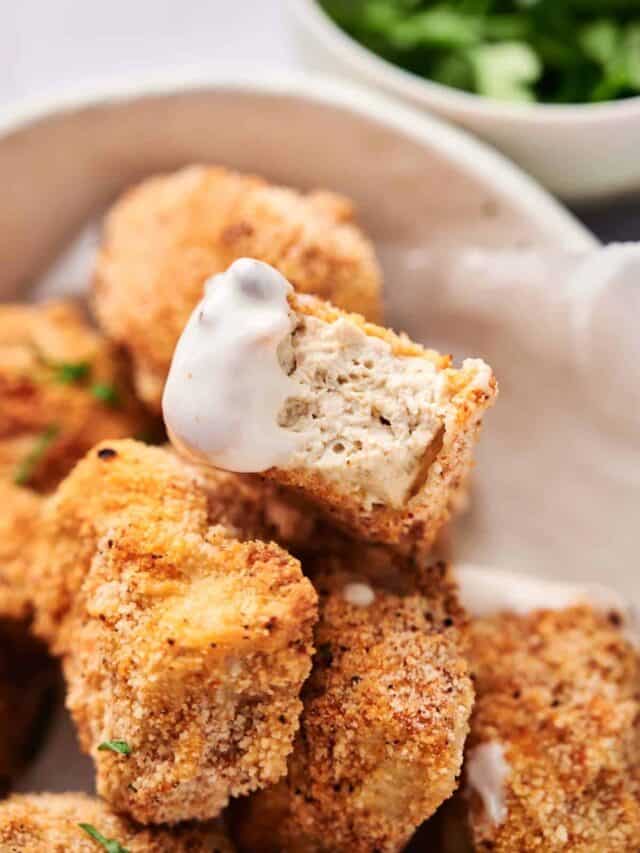 Breaded chicken nuggets with one piece dipped in creamy sauce.