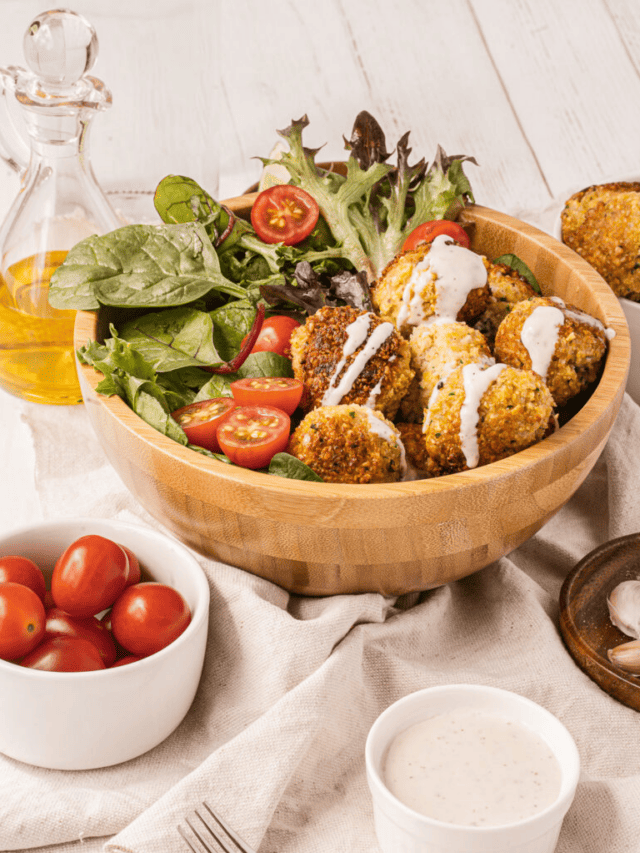 A bowl of falafel accompanied by fresh salad, cherry tomatoes, and a side of dressing with olive oil in the background.
