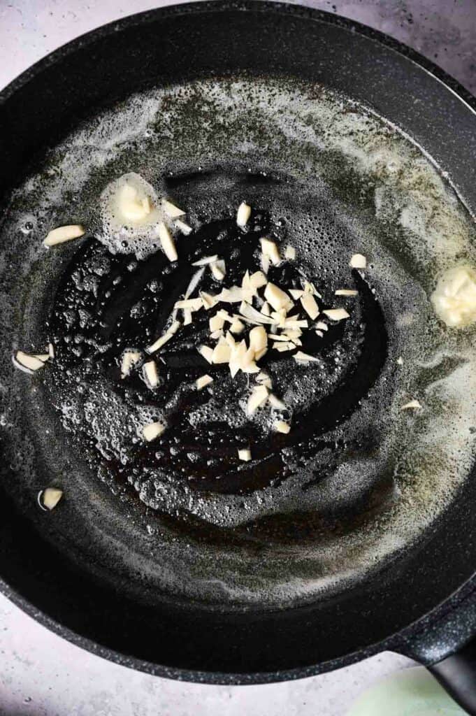 A skillet with melted butter, garlic slices, and chopped almonds, viewed from above.
