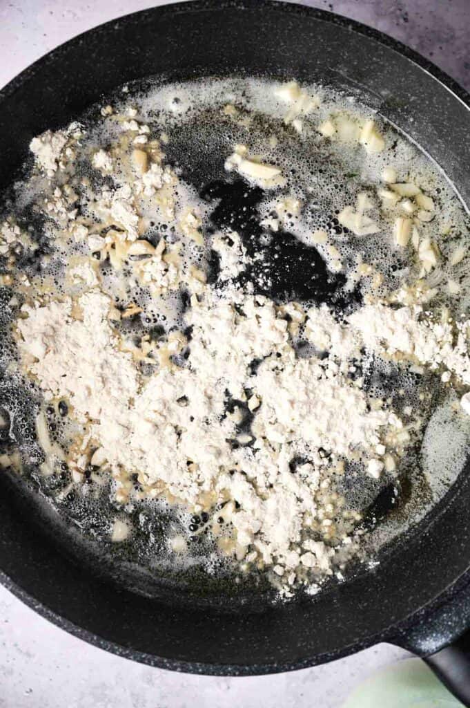 Cooking in a skillet with garlic and onions, oil visible, on a stovetop.