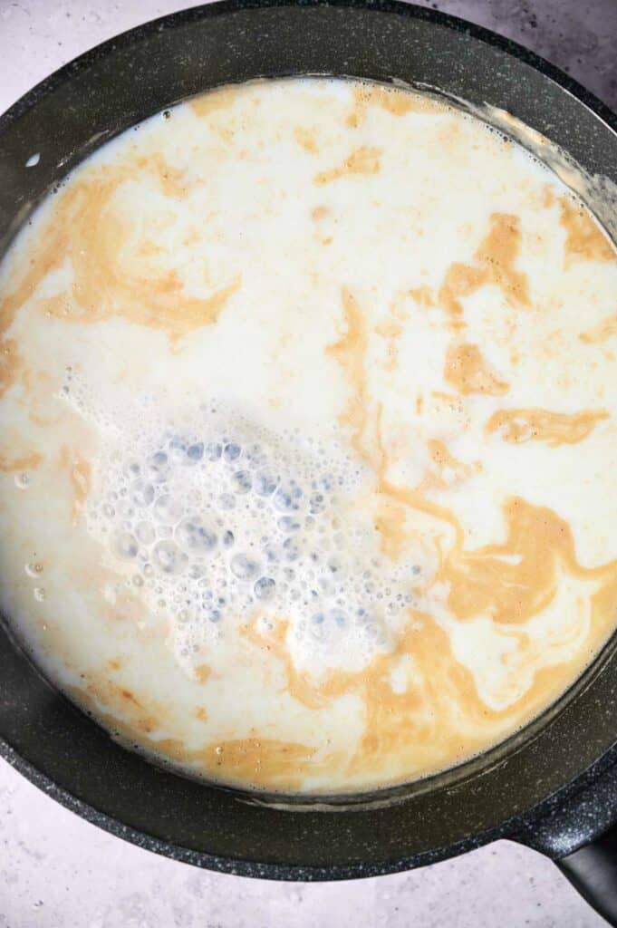 A skillet containing a mixture of milk, cooking on a stove, showing bubbles and slight browning.