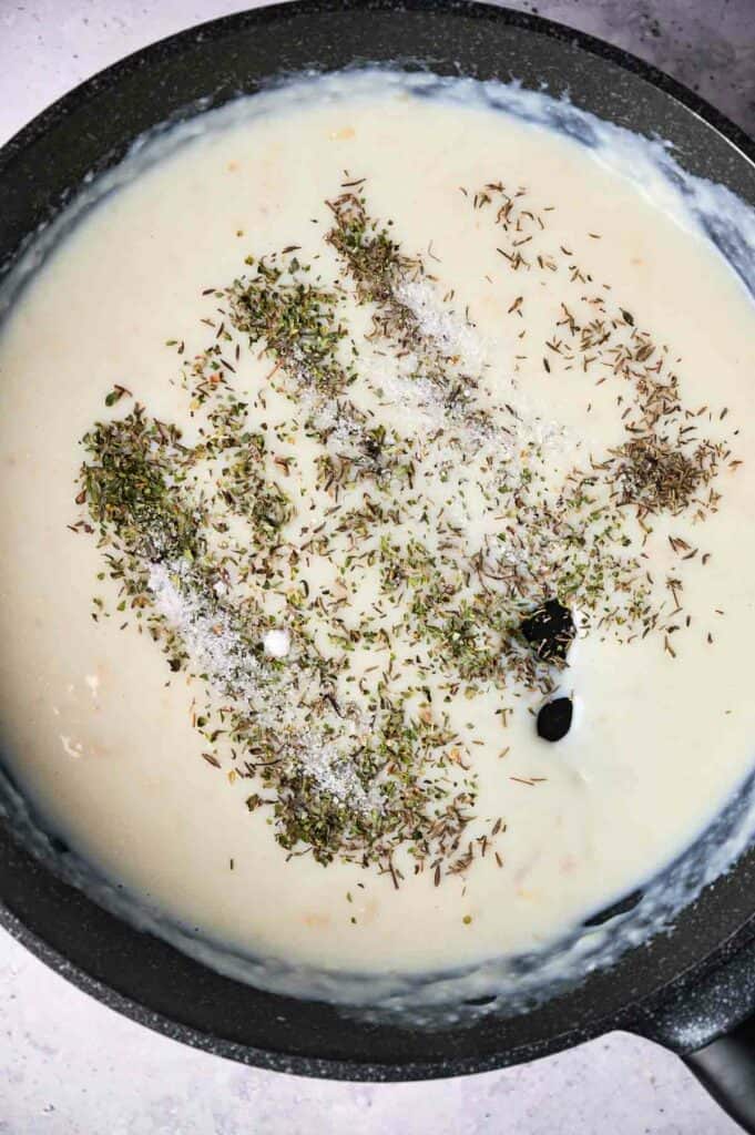 A skillet containing creamy soup garnished with herbs and spices on a marble surface.