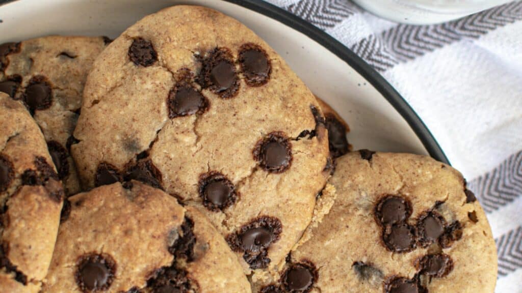 A plate of freshly baked chocolate chip cookies, with visible chunks of chocolate, on a striped cloth.
