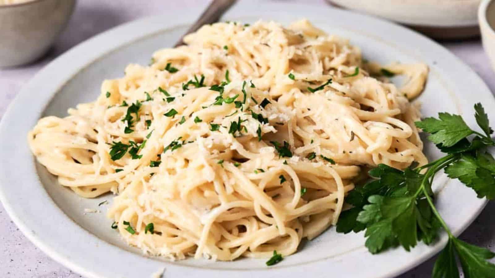 A plate of creamy fettuccine alfredo garnished with chopped parsley, served on a light-colored plate.