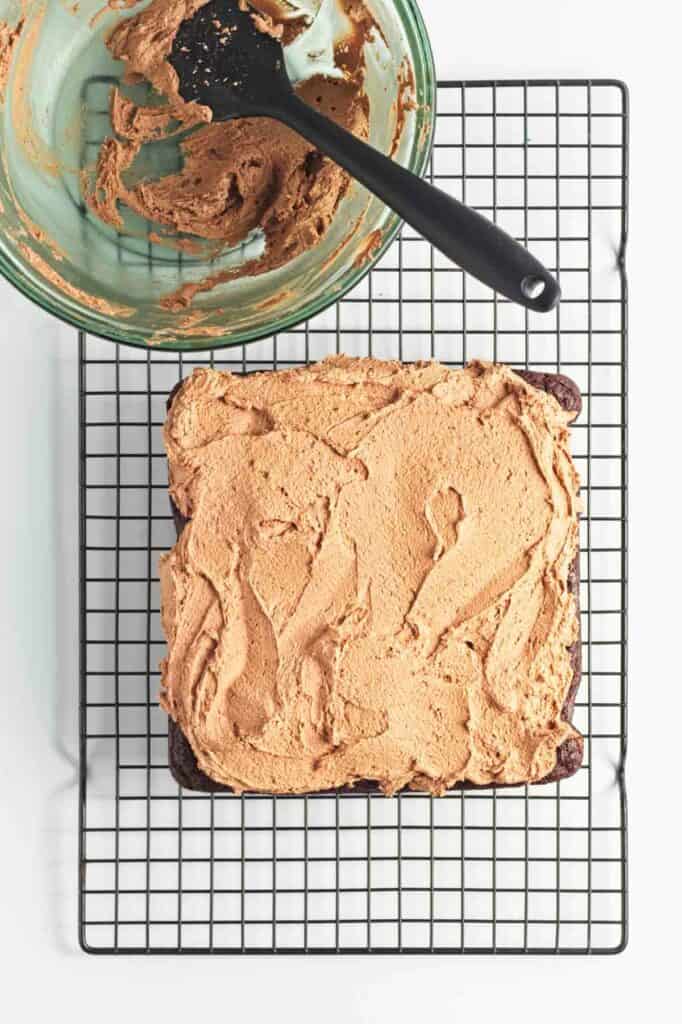 Vegan chocolate cake with a thick layer of peanut butter on a cooling rack, with a glass bowl and a knife.