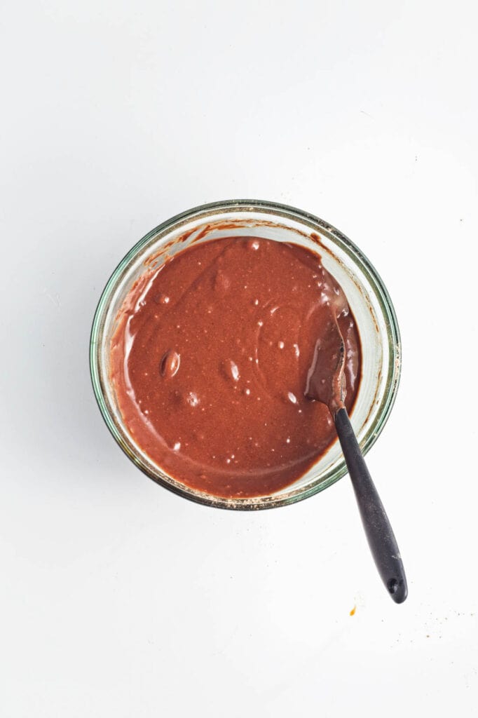 A bowl of vegan chocolate cake batter with a spoon inside, viewed from above.