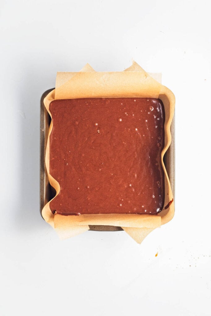 Unbaked vegan chocolate cake batter in a square pan lined with parchment paper.
