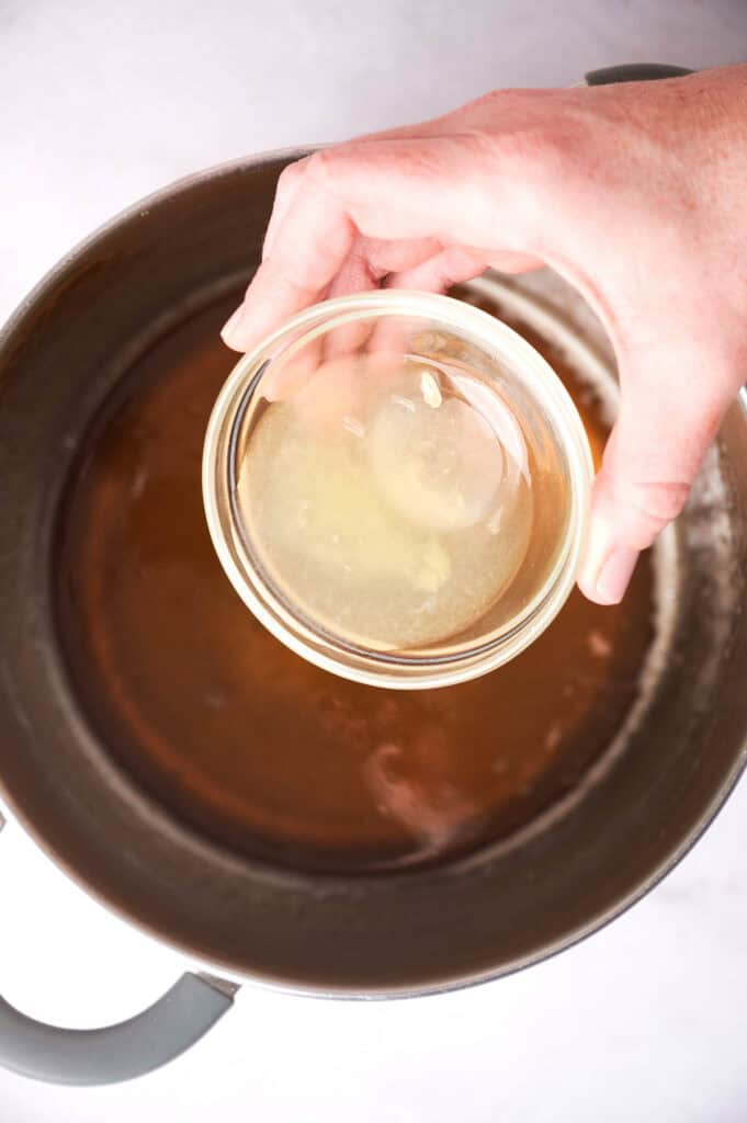 A person's hand holding a glass bowl with corn and maple syrup.