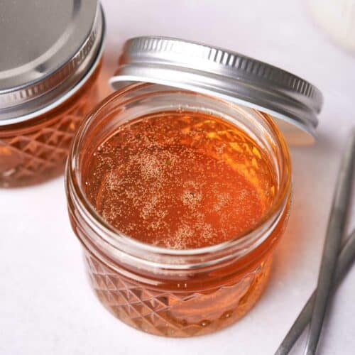 Two jars of vegan honey with metal lids on a white surface, one jar open displaying honey texture, accompanied by two spoons to the side.