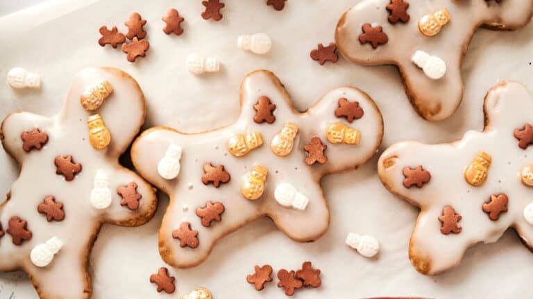 Gingerbread cookies with white icing, topped with small chocolate gingerbread men and snowman decorations, arranged on parchment paper.