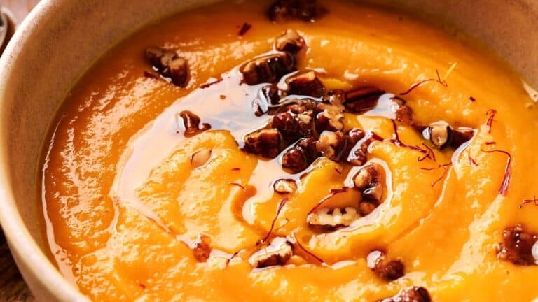 Close-up of a bowl of creamy vegan pumpkin soup, garnished with crunchy nuts and vibrant saffron threads.