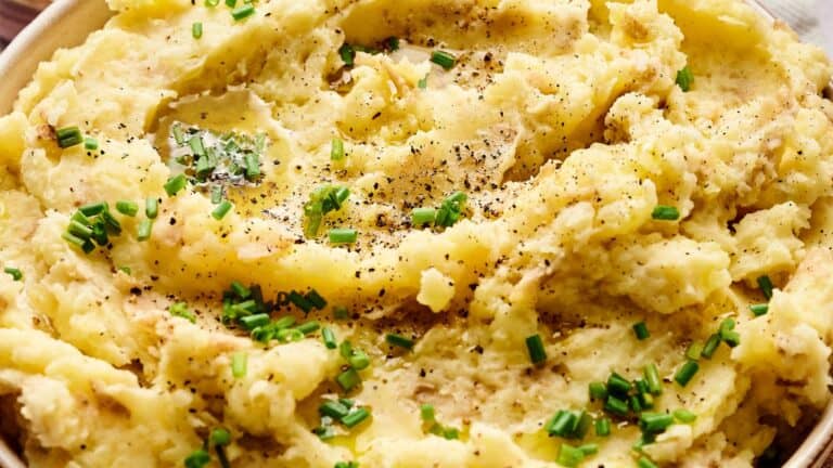 A bowl of mashed potatoes topped with chopped chives and black pepper.