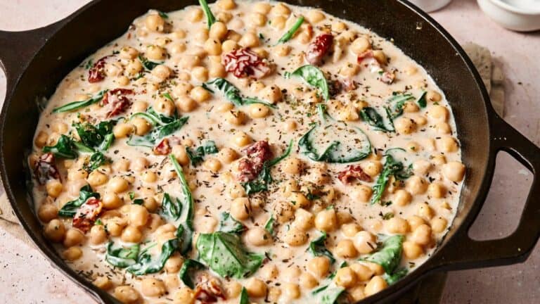 Skillet with creamy chickpeas, spinach, and sun-dried tomatoes, garnished with herbs.