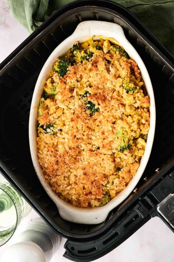 Inside a black air fryer basket, the vegan casserole dish boasts a golden brown breadcrumb topping, brimming with broccoli and rice.